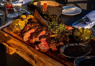 Sliced tomahawk steak with chimichurri, foil-baked potatoes and corn on the cob, served on a wooden board at the BBQ evening at Sunstar Hotel Klosters