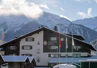 Verschneites Chalet-Hotel Sunstar in Klosters mit grünen Fensterläden, im Hintergrund schneebedeckte Gipfel und Wolken.