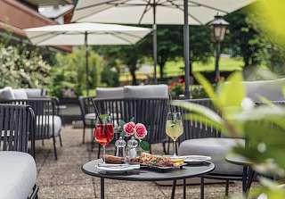 Summer terrace at the Sunstar Hotel Klosters with parasols and lounge chairs, with two summer drinks and an aperitif platter on the table
