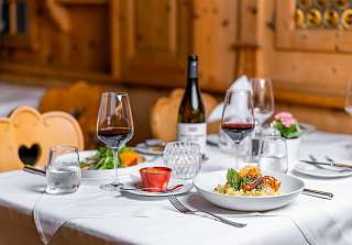 Set table with pasta, red wine and a wine bottle in a cosy restaurant at Sunstar Hotel Klosters