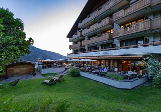 Clients profitant d'une soirée estivale sur la terrasse illuminée et dans le jardin du Sunstar Hotel Klosters avec vue sur les montagnes