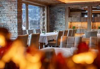 Tables élégamment dressées avec murs en pierre naturelle et poutres en bois dans l'espace restaurant du Sunstar Hotel Klosters