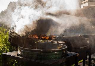 Bacon-wrapped sausages smoking on the Big Green Egg at the BBQ evening at Sunstar Hotel Klosters, mountains in the background