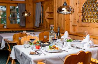 Gedeckter Tisch mit regionalem Gericht und Rotwein im rustikalen Bereich der Boscastube des Sunstar Hotels Klosters