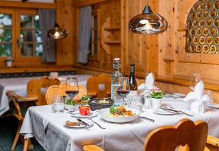 Gedeckter Tisch mit regionalem Gericht und Rotwein im rustikalen Bereich der Boscastube des Sunstar Hotels Klosters