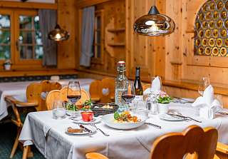 Table dressée avec plat régional et vin rouge dans l'espace rustique de la Bosca Stube du Sunstar Hotel Klosters