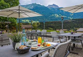Gedeckter Tisch mit Salat und Orangensaft auf der Sonnenterrasse des Sunstar Hotels Klosters mit Blick auf die Bündner Bergwelt