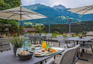 Table dressée avec salade et jus d'orange sur la terrasse ensoleillée du Sunstar Hotel Klosters avec vue sur les montagnes des Grisons