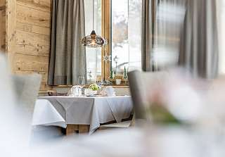 Atmospherically set table by the window with winter decoration and pendant light in the Boscastube at Sunstar Hotel Klosters