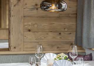 Close-up of a laid table with wine glasses and folded napkins in front of a reclaimed wood wall with a glass pendant light in the Bosca Stube