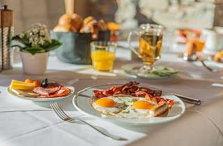 Frisch zubereitete Spiegeleier mit Bacon, Aufschnitt und Orangensaft beim Frühstück im Sunstar Hotel Klosters