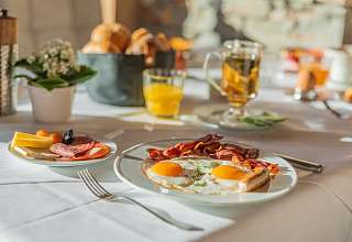 Frisch zubereitete Spiegeleier mit Bacon, Aufschnitt und Orangensaft beim Frühstück im Sunstar Hotel Klosters
