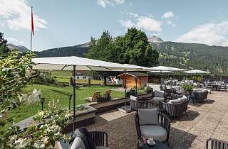 Weitläufige Sonnenterrasse mit Lounge-Möbeln, Sonnenschirmen und Blick auf den Gotschnagrat im Sunstar Hotel Klosters