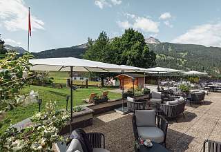 Weitläufige Sonnenterrasse mit Lounge-Möbeln, Sonnenschirmen und Blick auf den Gotschnagrat im Sunstar Hotel Klosters