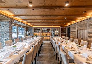 Zwei parallel gedeckte Tischreihen mit weissen Tischdecken und Natursteinwand im Saal Boscablick des Sunstar Hotels Klosters
