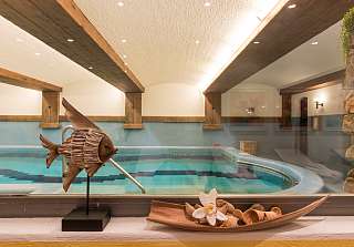 Tranquil indoor pool in the wellness area of Sunstar Hotel Klosters, with wooden beams, warm lighting and decorative elements in the foreground.